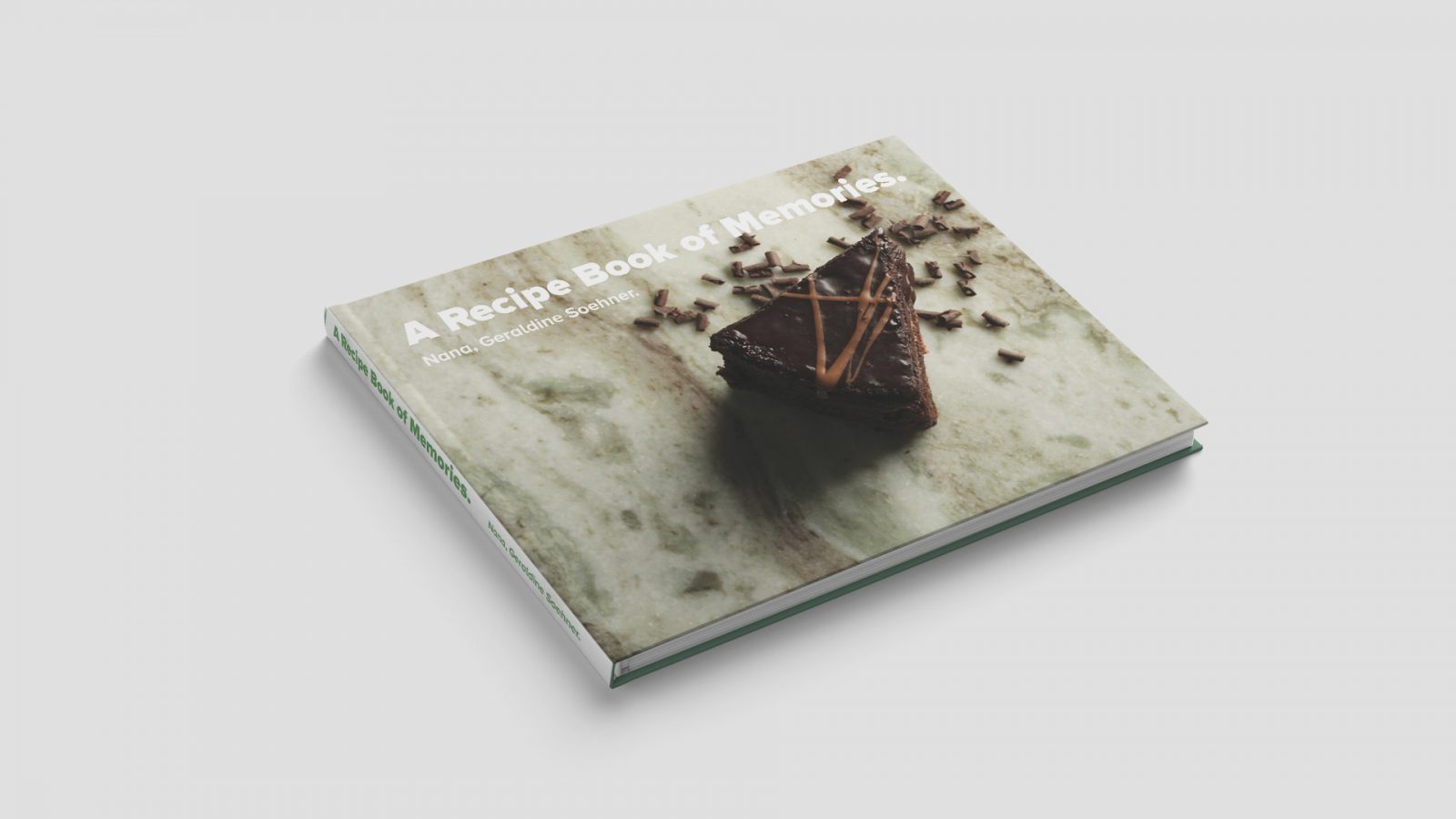 An image of a “A Recipe Book of Memories” that is 10 inches by 13 inches featuring a dark brown chocolate cake on a piece of green and white marbled granite. The chocolate cake is surrounded by chocolate shavings with the title of “A Recipe Book of Memories” scaled across the top of the book.