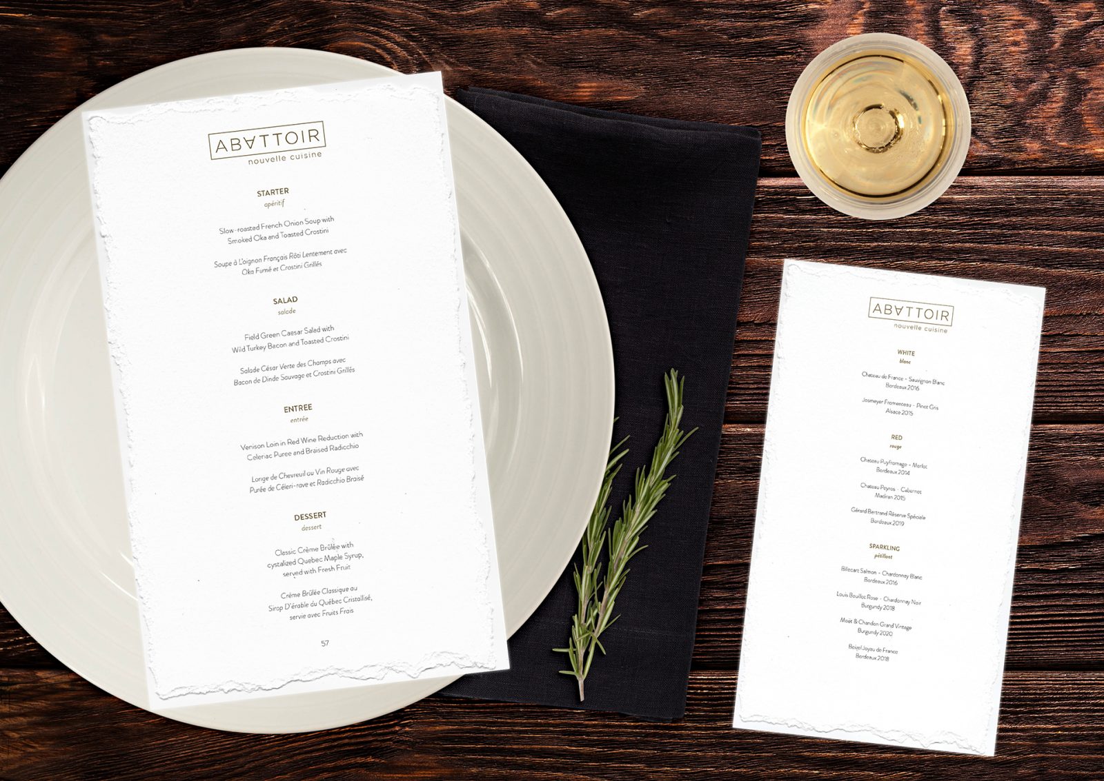 Seasonal 4 course meal menu design for Abattoir Nouvelle Cuisine. This image shows a textured paper menu over a fine dining place setting on a wood table. It has a smaller textured paper wine menu on the right side of the place setting. The typography is centre aligned in both English and French underneath the gold wordmark logo.