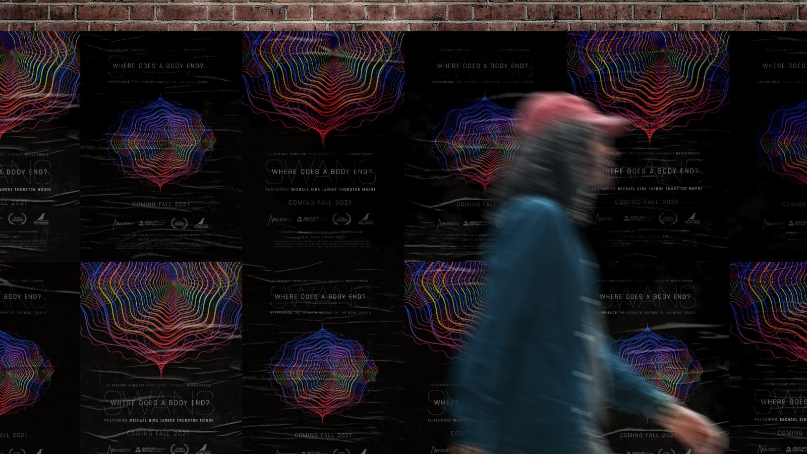 This image shows the main graphic for the mock advertising campaign for the documentary film Swans: Where Does a Body End? in context. The main graphic is a glowing organic orb made up of technicolour streams. A man walks by a wild hoarding of posters that are tiled horizontally across a brick wall. The posters show what the main graphic paired with minimalistic typography which showcases the film’s name and release date. The posters showcase two versions of the main graphic one that is zoomed in and one is further way.