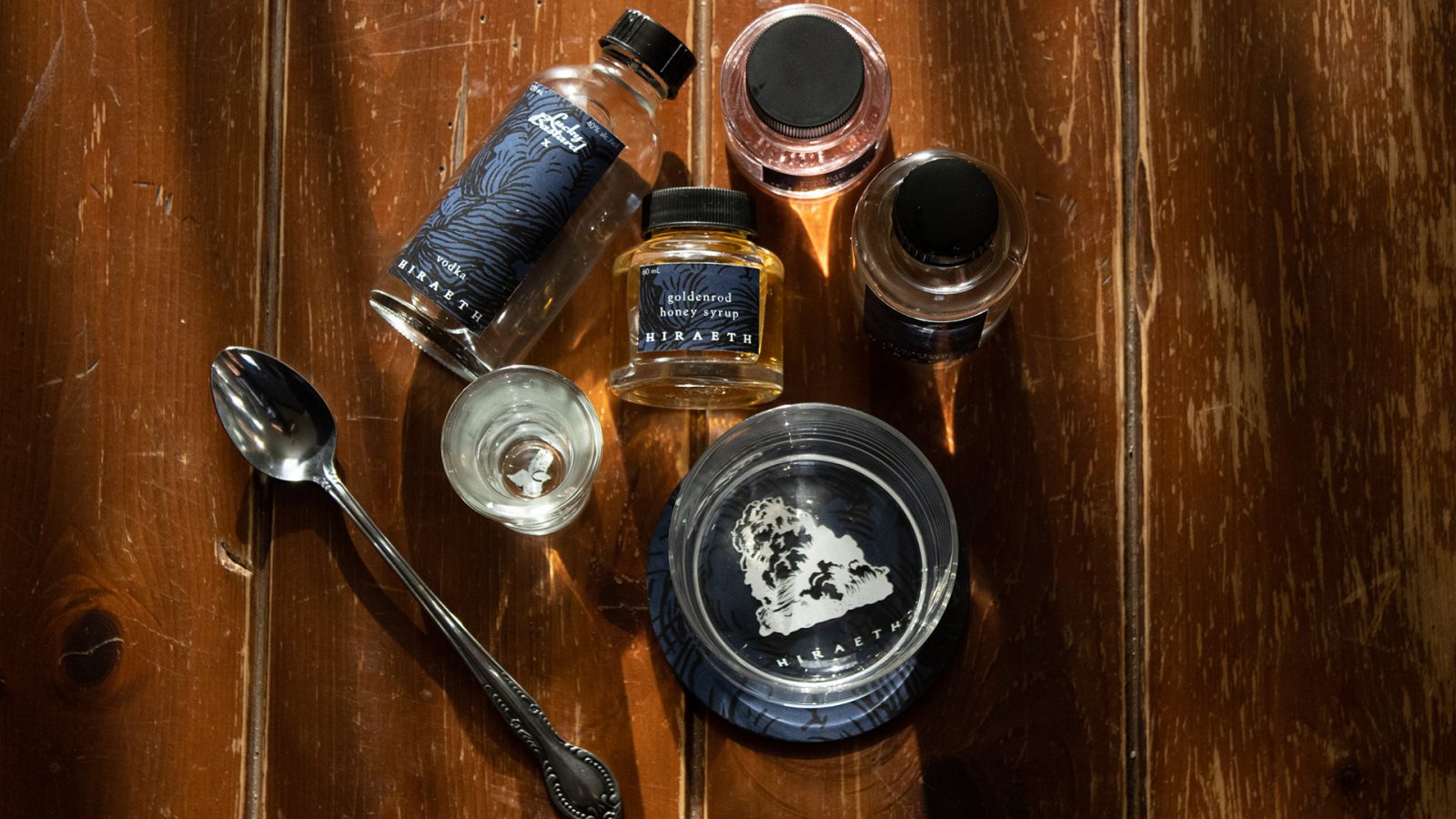 Various pieces of an at-home cocktail kit are strewn on a rough wooden table.