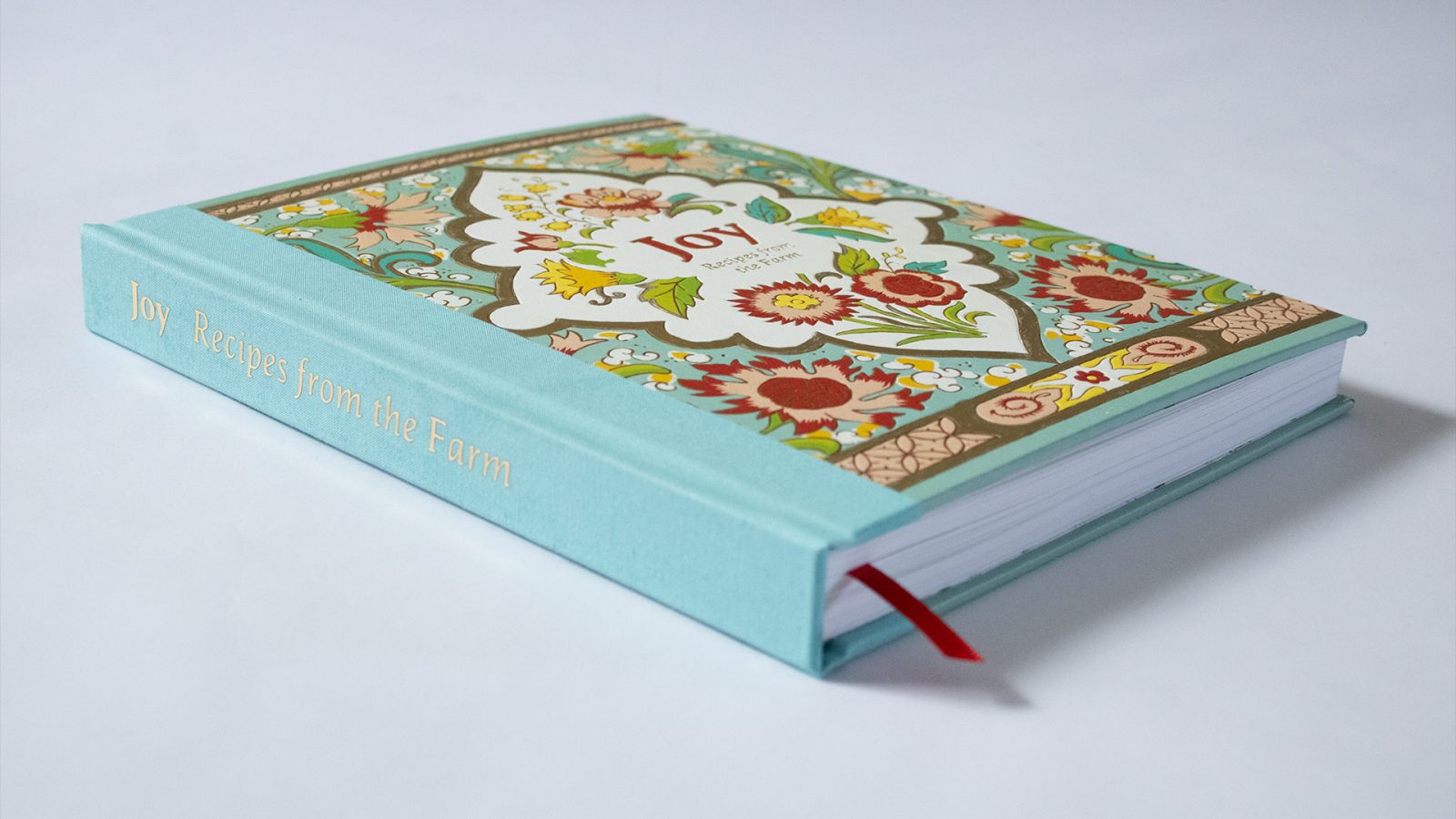 A three-quarter view of heavily decorated cookbook with the title in gold foil on the spine sitting on a neutral background.